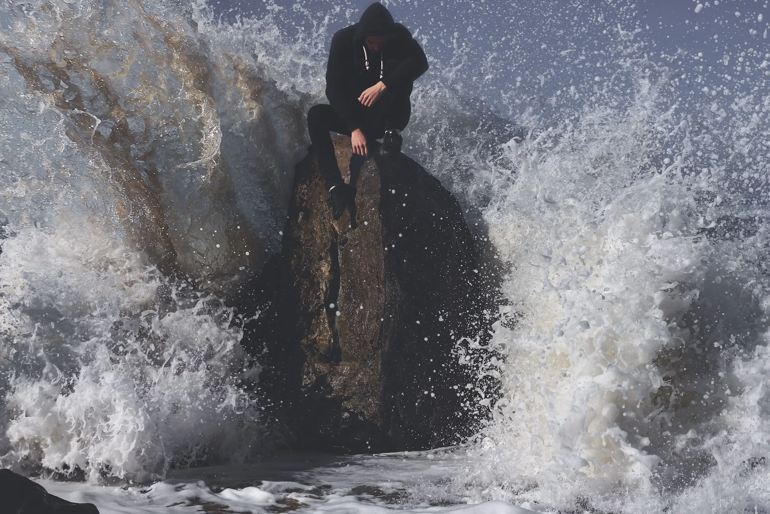 Uomo seduto su uno scoglio travolto dalle onde del mare